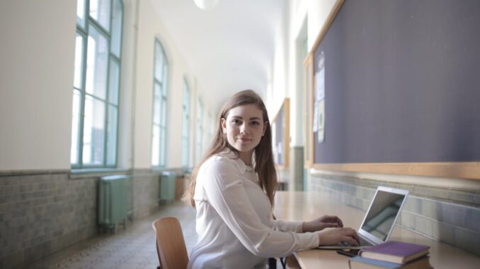 Female student typing on laptop in university hallway