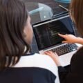 Two Women Looking at the Code at Laptop