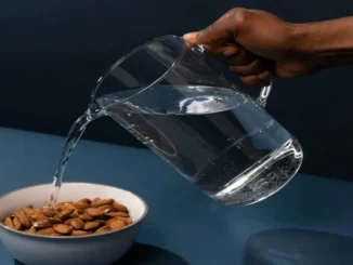 A white bowl containing five soaked and peeled almonds placed on a wooden table.