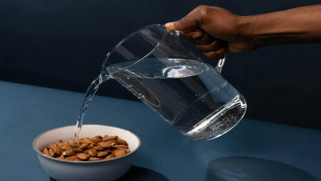 A white bowl containing five soaked and peeled almonds placed on a wooden table.