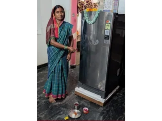 Hanumamma from Sindhanur smiling next to her new refrigerator purchased with Gruha Lakshmi savings.