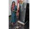 Hanumamma from Sindhanur smiling next to her new refrigerator purchased with Gruha Lakshmi savings.
