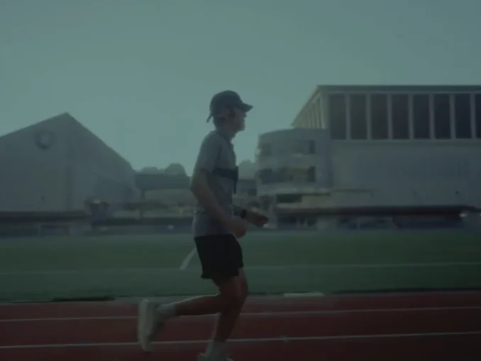A low-vision athlete testing the Google DeepMind Running Guide agent while running on an outdoor track with a chest-mounted Pixel device.