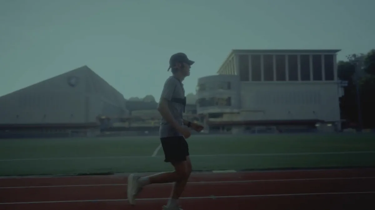 A low-vision athlete testing the Google DeepMind Running Guide agent while running on an outdoor track with a chest-mounted Pixel device.